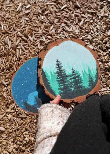 Painted wood slices with nature scenes outdoors.