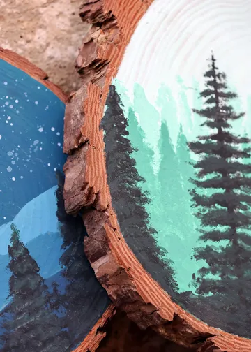 Painted wood slices with forest scenes.