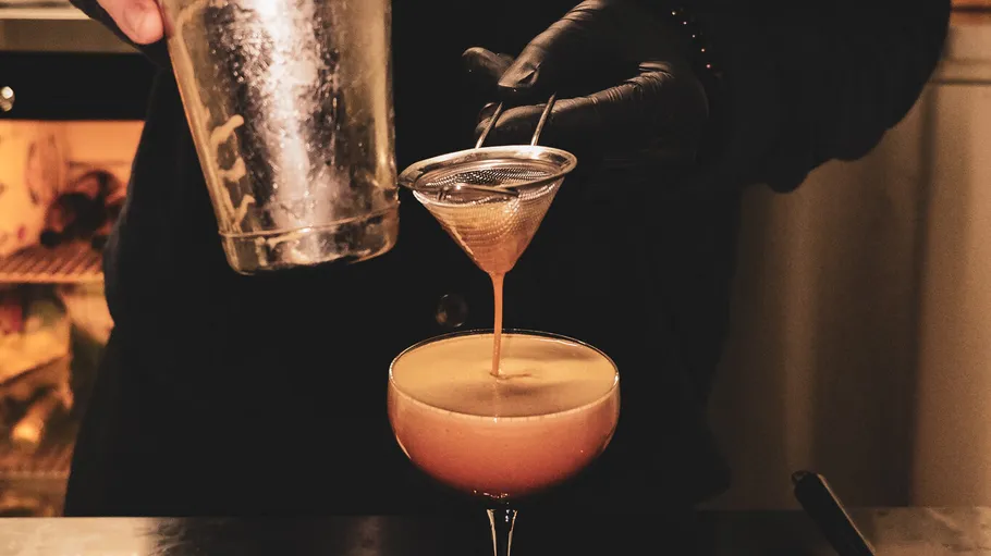 Bartender straining cocktail into a glass.