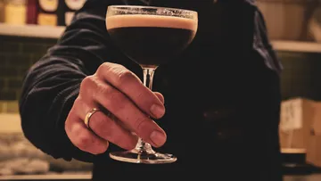 Hand hält Espresso Martini in Bar.