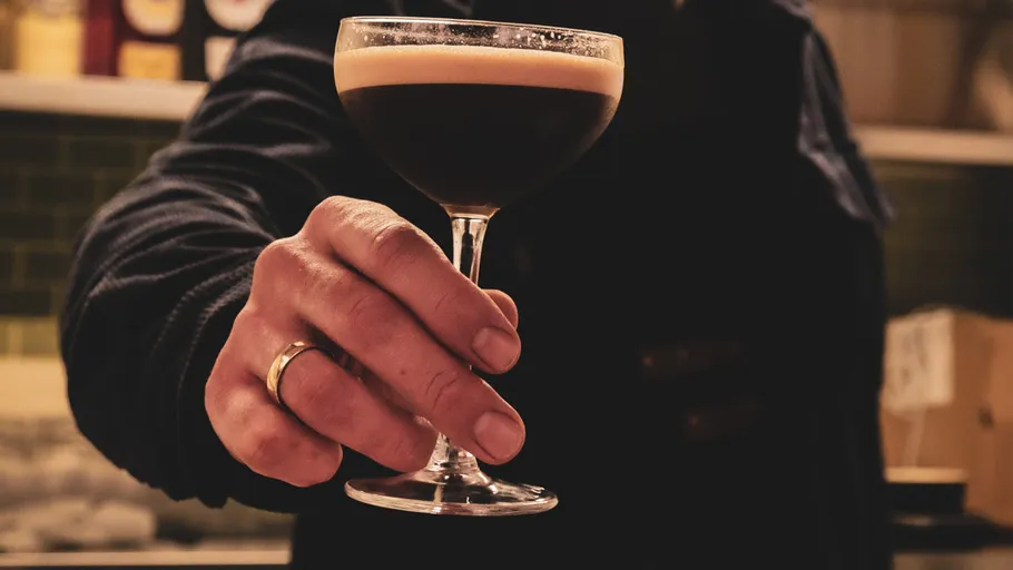 Hand holding espresso martini in bar.