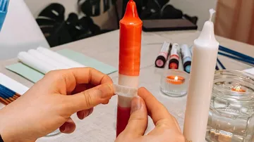 Hands decorating candles on a table.