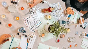 Hands crafting candles on a table.