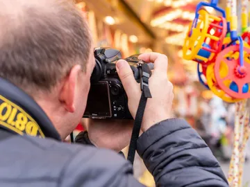 Mann fotografiert mit Kamera bunte Spielzeuge im Hintergrund.