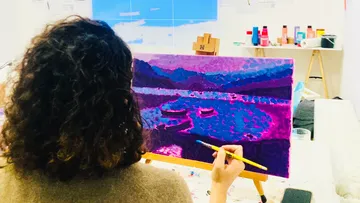 Person painting colorful landscape on canvas indoors.
