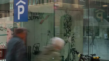 Menschen gehen an Parkschild und Glasgebäude vorbei.