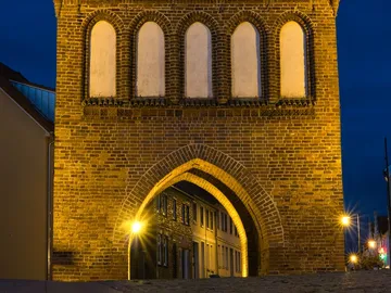 Historic gate glows at night, the surrounding street is illuminated.
