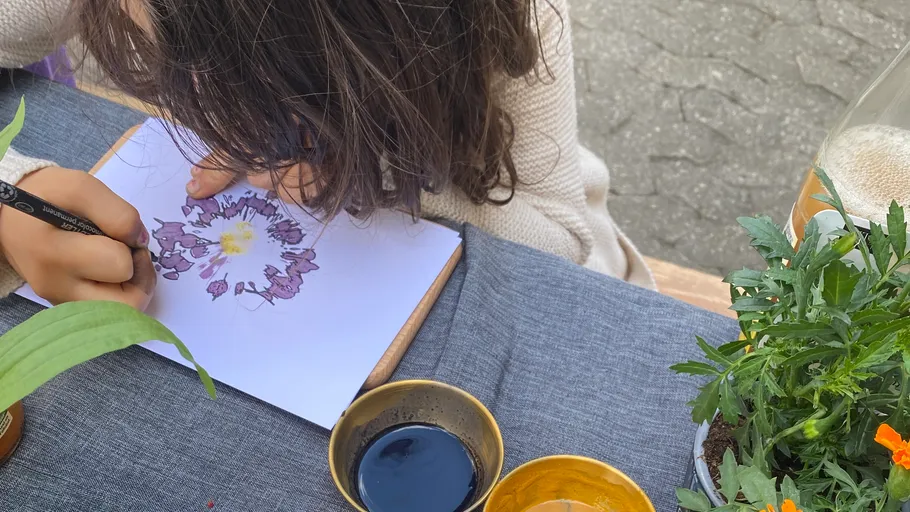 Kind zeichnet Blume am Tisch im Freien.