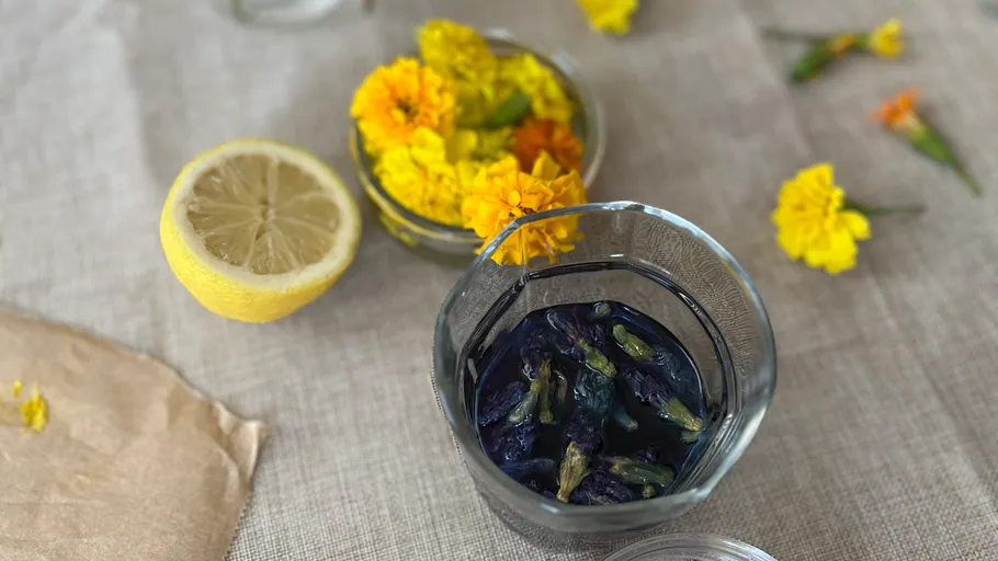 Glas mit blauen Blumen, Zitrone und Ringelblumen in der Nähe.