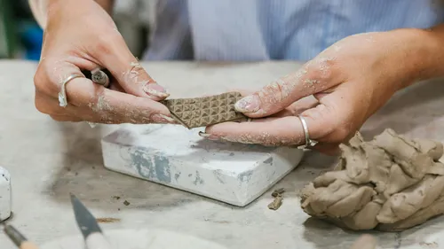 Hands shaping clay with texture pattern.