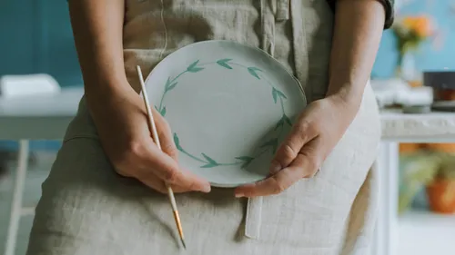 Person holding painted ceramic plate in studio.
