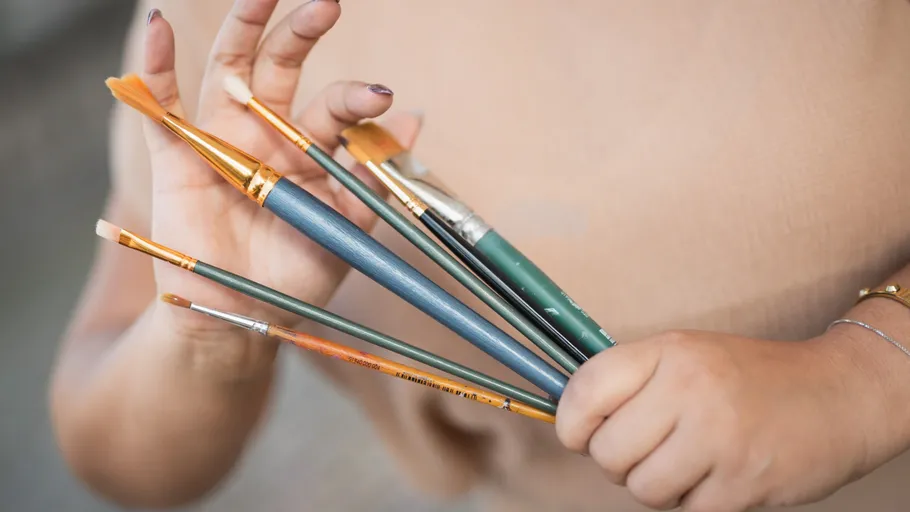 Hand hält verschiedene Pinsel, unscharfer Hintergrund.