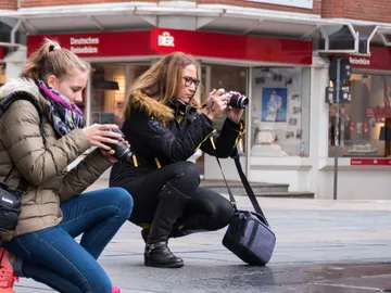 Two photographers kneel and take pictures on the street.