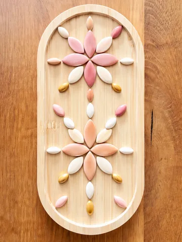 Bunte Fliesen bilden Blumenmuster auf Holz.