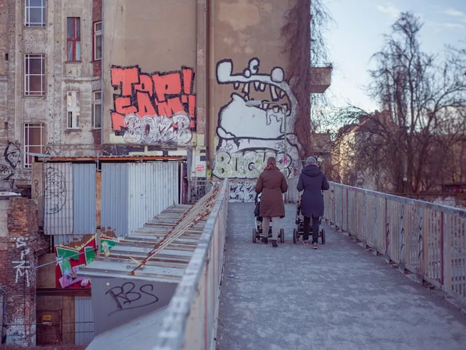 Two women are walking across a bridge with a stroller.