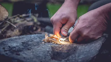 Hände entzünden Feuer auf Stein mit Zunder.