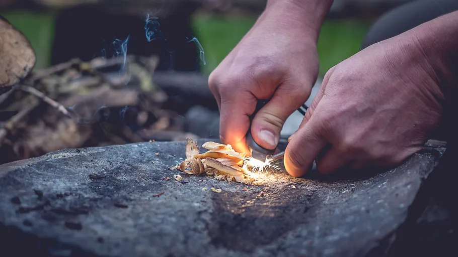 Hands starting fire on rock with tinder.