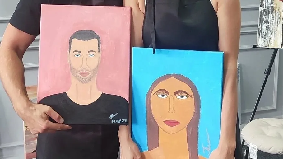 People holding two painted portraits indoors.