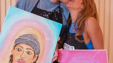Couple kissing, holding painted portraits.
