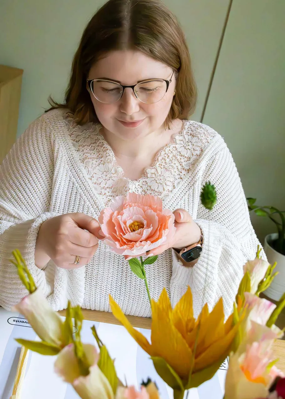 Woman crafting paper flower at table.