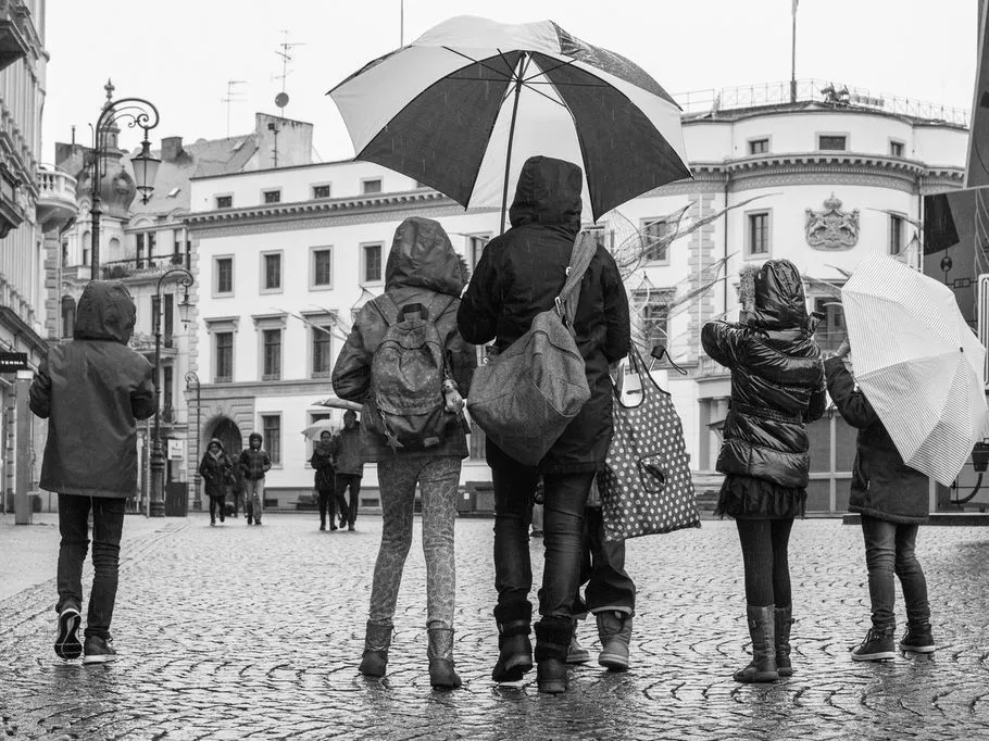 Fünf Personen gehen bei Regen mit Regenschirmen.