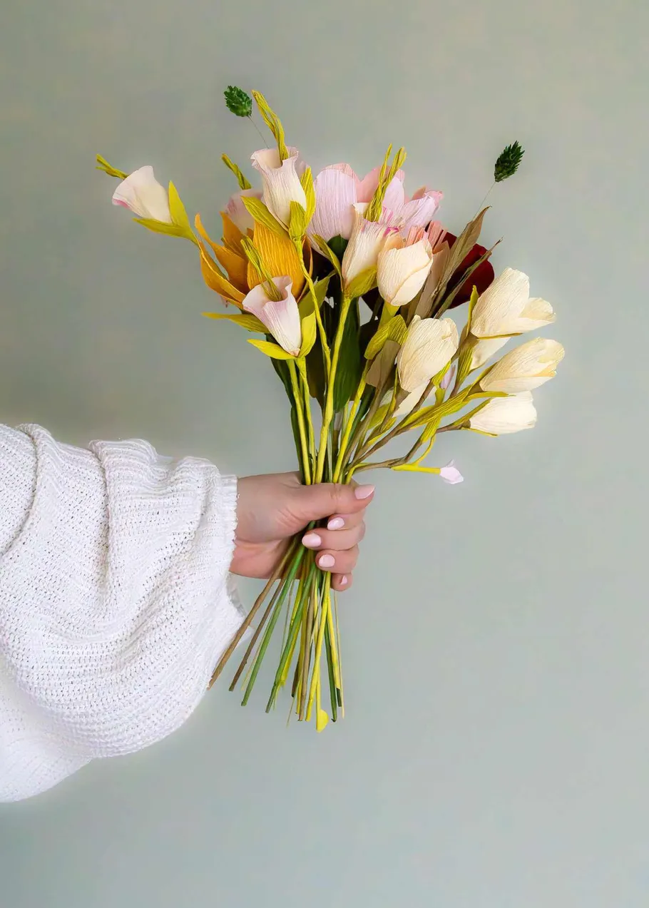 Hand holding colorful flower bouquet indoors.