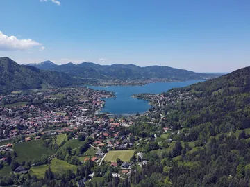 Bergsee spiegelt Himmel, umgeben von grünen Hügeln und Dörfern.