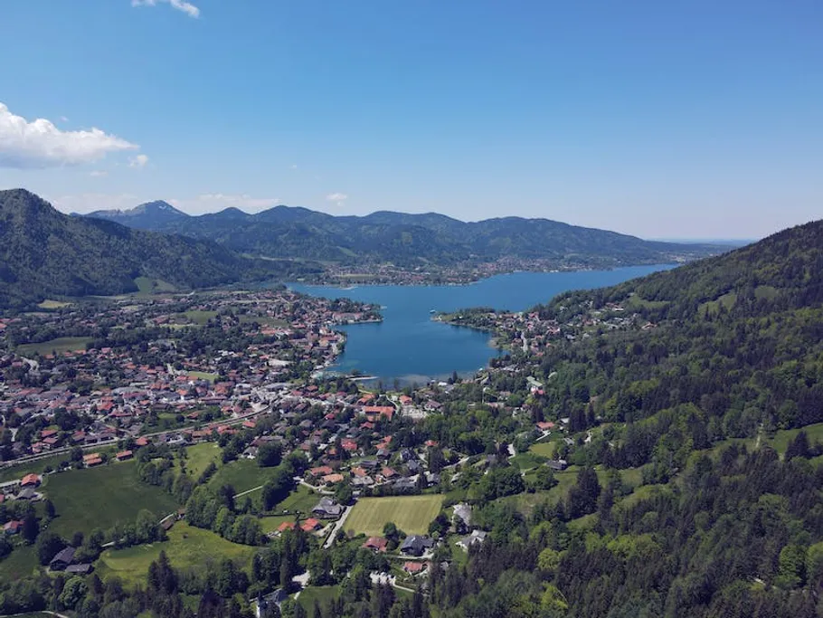 Mountain lake reflects sky surrounded by green hills and villages.