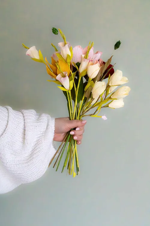 Hand hält bunter Papierblumenstrauß.