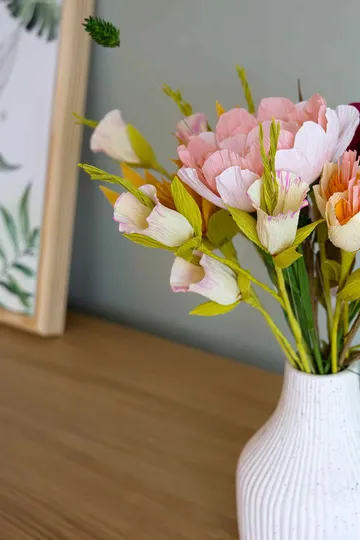 Papierblumen in Vase auf Holztisch.