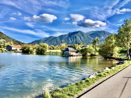 Quiet lake surrounded by mountains and trees, sunny sky.