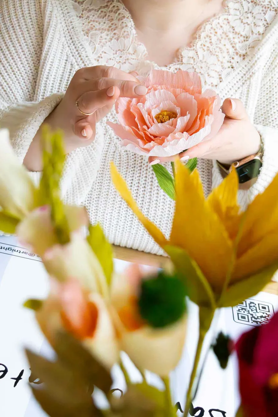 Hands holding pink artificial flower, table setting.