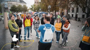 Reiseleiter spricht zu Gruppe auf Stadtplatz.