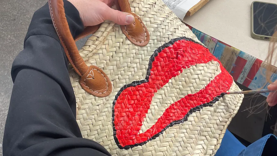 Person malt Lippen auf geflochtener Handtasche.