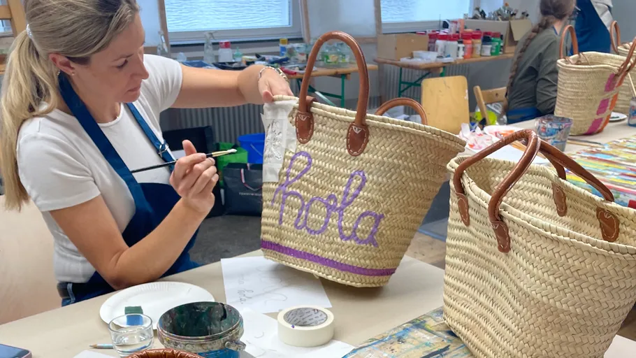 Woman painting on woven bag in workshop.