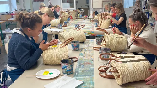 Frauen bemalen Strohtaschen in einem Workshop.