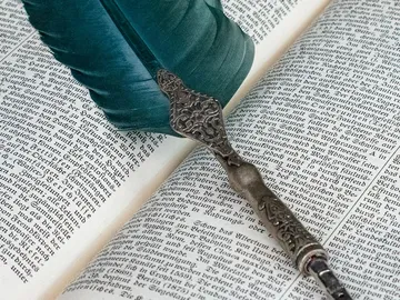 Feder und Tinte liegen auf geöffnetem Buchseiten.
