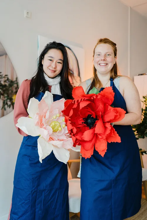 Two women holding giant paper flowers indoors.