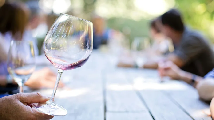 Wine glass held over outdoor table gathering.