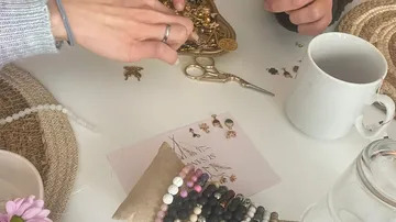Hände arrangieren Schmuck auf Tisch mit Tasse.