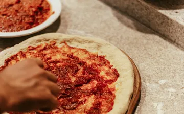 Hand verteilt Soße auf Pizzateig.