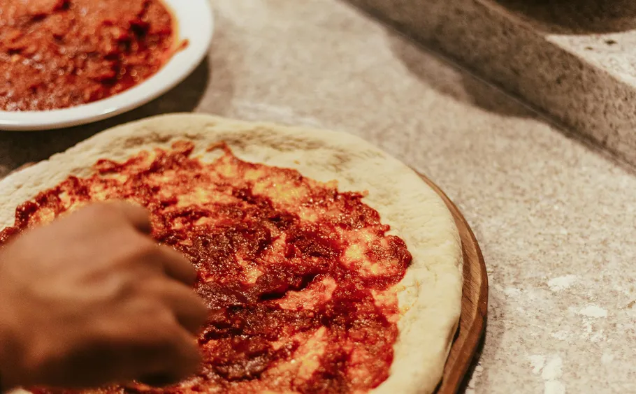 Hand spreading sauce on pizza dough.
