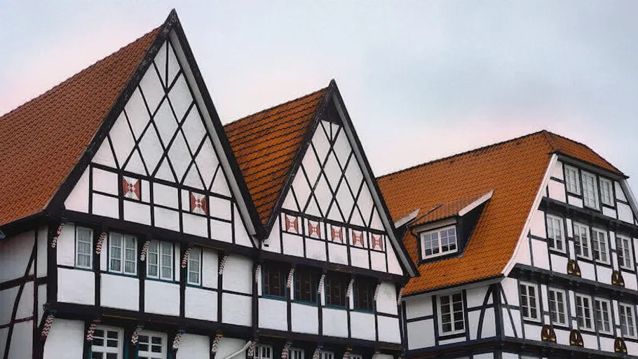 Half-timbered houses with red roofs, cloudy sky.