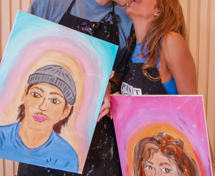 Couple kissing while holding painted portraits.