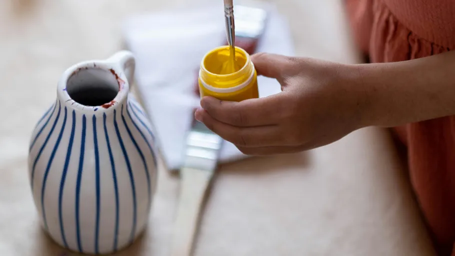 Person dipping brush into yellow paint jar.