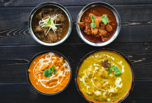 Four bowls of colorful curry on dark wood.