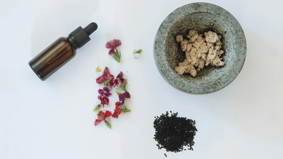 Dropper bottle, flowers, seeds, and mortar on white background.