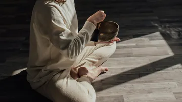 Person playing singing bowl on wooden floor.