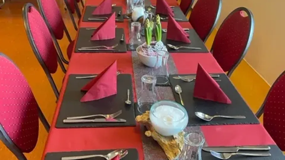 Tisch mit roten Servietten und Stühlen gedeckt.