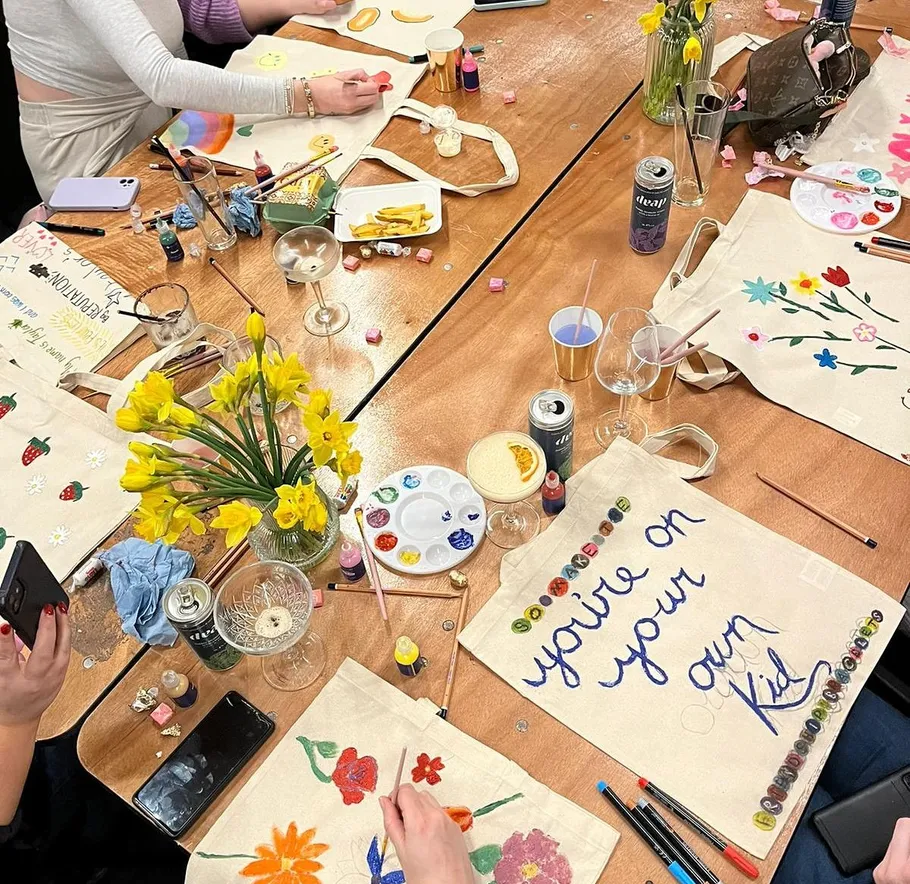 People painting tote bags at a table.